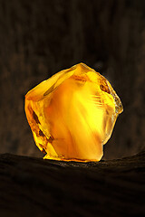 Image showing Beauty of natural raw amber. A piece of yellow opaque natural amber on large piece of dark stoned wood.