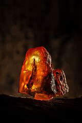 Image showing Beauty of natural raw amber. A piece of yellow-red transparent natural amber on piece of stoned wood