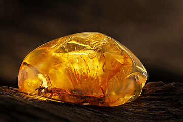 Image showing Beauty of natural raw amber. A piece of yellow transparent natural amber on piece of stoned wood