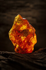 Image showing Beauty of natural raw amber. A piece of yellow-red transparent natural amber on piece of stoned wood