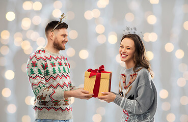 Image showing happy couple in ugly sweaters with christmas gift