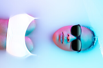 Image showing Beautiful female face in the milk bath with soft glowing in blue-pink neon light