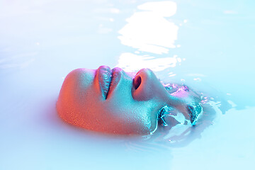 Image showing Beautiful female face in the milk bath with soft glowing in blue-pink neon light