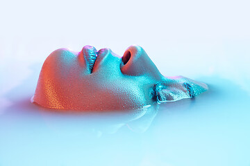 Image showing Beautiful female face in the milk bath with soft glowing in blue-pink neon light