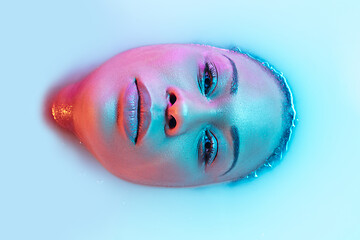 Image showing Beautiful female face in the milk bath with soft glowing in blue-pink neon light