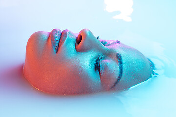 Image showing Beautiful female face in the milk bath with soft glowing in blue-pink neon light