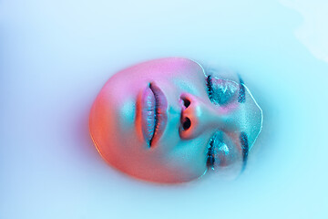 Image showing Beautiful female face in the milk bath with soft glowing in blue-pink neon light