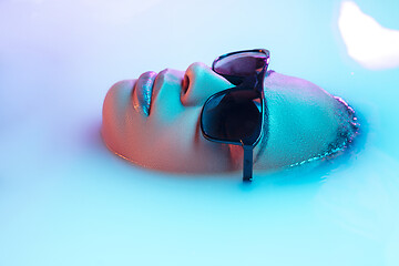 Image showing Beautiful female face in the milk bath with soft glowing in blue-pink neon light