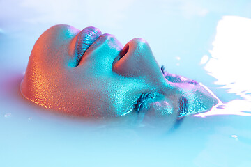 Image showing Beautiful female face in the milk bath with soft glowing in blue-pink neon light