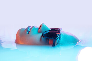 Image showing Beautiful female face in the milk bath with soft glowing in blue-pink neon light