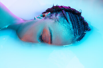 Image showing Beautiful female face in the milk bath with soft glowing in blue-pink neon light