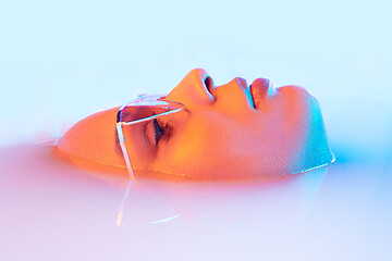 Image showing Beautiful female face in the milk bath with soft glowing in blue-pink neon light