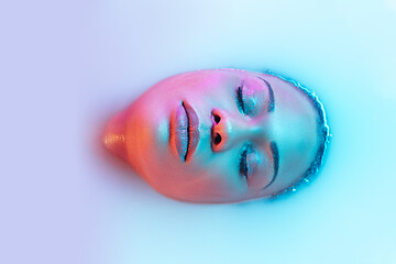 Image showing Beautiful female face in the milk bath with soft glowing in blue-pink neon light