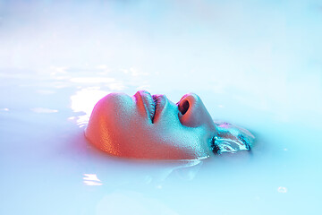 Image showing Beautiful female face in the milk bath with soft glowing in blue-pink neon light