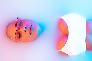 Image showing Beautiful female face in the milk bath with soft glowing in blue-pink neon light