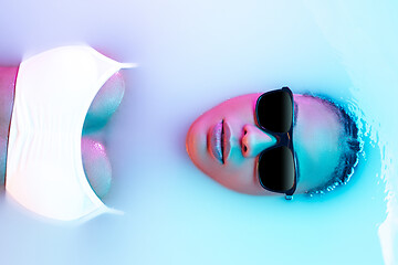 Image showing Beautiful female face in the milk bath with soft glowing in blue-pink neon light