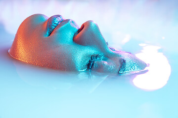 Image showing Beautiful female face in the milk bath with soft glowing in blue-pink neon light