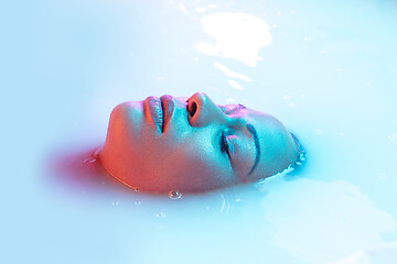 Image showing Beautiful female face in the milk bath with soft glowing in blue-pink neon light