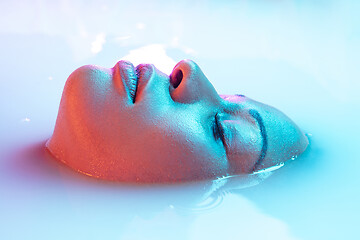 Image showing Beautiful female face in the milk bath with soft glowing in blue-pink neon light