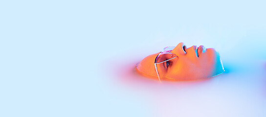 Image showing Beautiful female face in the milk bath with soft glowing in blue-pink neon light