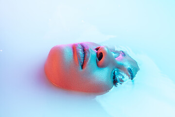 Image showing Beautiful female face in the milk bath with soft glowing in blue-pink neon light