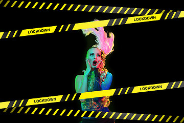 Image showing Beautiful young woman in carnival, stylish masquerade costume with feathers behind limiting tapes with word Lockdown