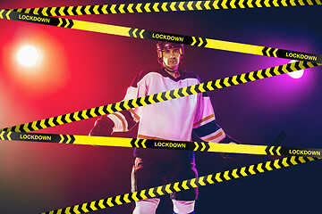 Image showing Male hockey player wearing equipment, helmet posing on gradient background behind limiting tapes with word Lockdown