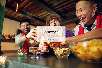 Image showing Excited, shocked soccer fans cheering for favourite sport team in restaurant or bar behind the message with word Lockdown