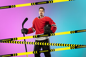 Image showing Male hockey player wearing equipment, helmet posing on gradient background behind limiting tapes with word Lockdown