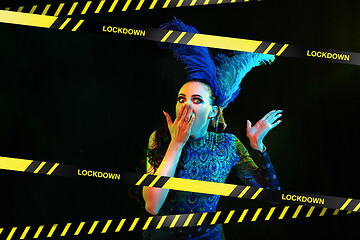 Image showing Beautiful young woman in carnival, stylish masquerade costume with feathers behind limiting tapes with word Lockdown