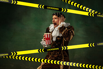 Image showing Medieval young man in old-fashioned costume with popcorn behing the limiting tapes with word Lockdown