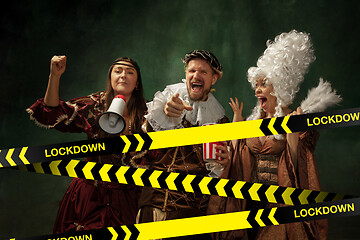 Image showing Medieval young man and women in old-fashioned costume with popcorn behing the limiting tapes with word Lockdown