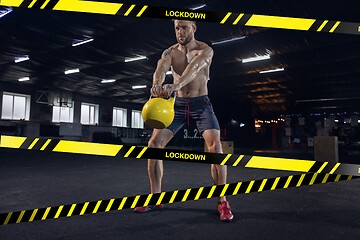 Image showing Young sportive man training on gym background behind limiting tapes with word Lockdown