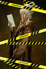 Image showing Medieval young woman in old-fashioned costume with tablet behing the limiting tapes with word Lockdown