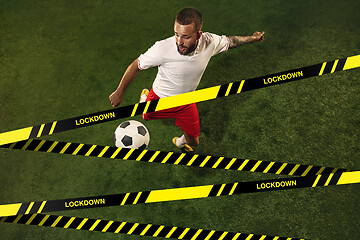 Image showing Football or soccer player on grass background behind limiting tapes with word Lockdown