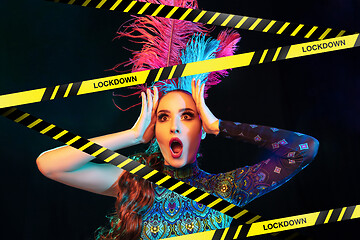 Image showing Beautiful young woman in carnival, stylish masquerade costume with feathers behind limiting tapes with word Lockdown