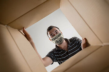 Image showing Young man in face mask with sign masks for 100 days in USA opening the biggest postal package
