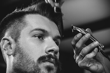 Image showing Young handsome barber making haircut for attractive man in barbershop