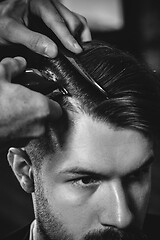 Image showing Young handsome barber making haircut for attractive man in barbershop