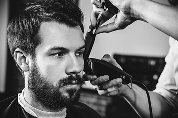 Image showing Young handsome barber making haircut for attractive man in barbershop