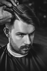 Image showing Young handsome barber making haircut for attractive man in barbershop