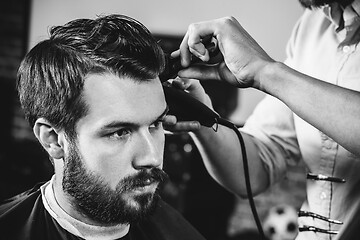 Image showing Young handsome barber making haircut for attractive man in barbershop