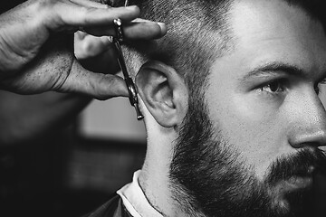 Image showing Young handsome barber making haircut for attractive man in barbershop