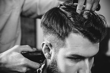 Image showing Young handsome barber making haircut for attractive man in barbershop