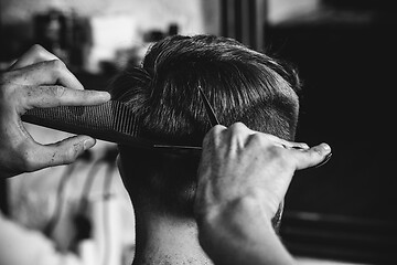 Image showing Young handsome barber making haircut for attractive man in barbershop