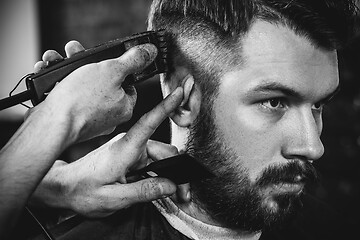 Image showing Young handsome barber making haircut for attractive man in barbershop