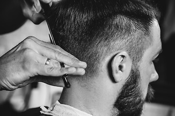 Image showing Young handsome barber making haircut for attractive man in barbershop