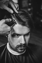 Image showing Young handsome barber making haircut for attractive man in barbershop