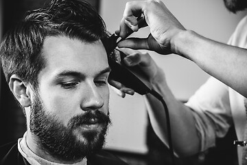 Image showing Young handsome barber making haircut for attractive man in barbershop