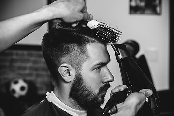 Image showing Young handsome barber making haircut for attractive man in barbershop